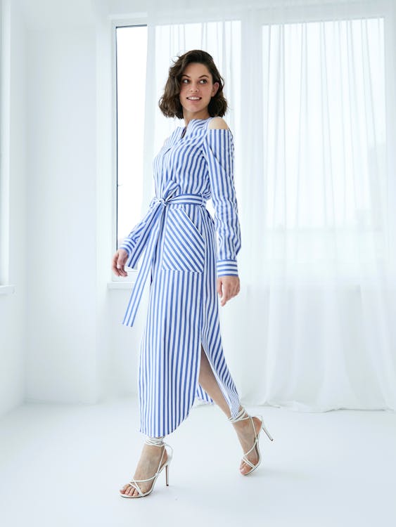 Free Woman in Dress with Blue Stripes Walking in White Room Stock Photo